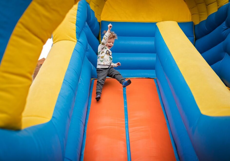 Here's an alt tag for the image: Happy toddler sliding down bouncy castle.
